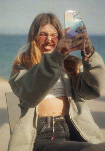 Young woman with sunglasses, a smartphone with charm and colorful body chain